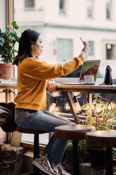 Full length side view of female blogger taking selfie sitting at cafe - MASF00473