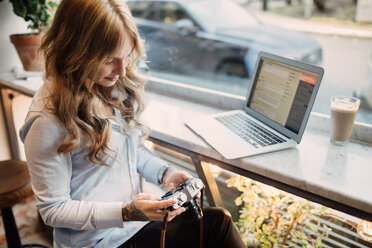 Hohe Winkel Ansicht der jungen Frau hält Kamera beim Sitzen mit Laptop im Café - MASF00475