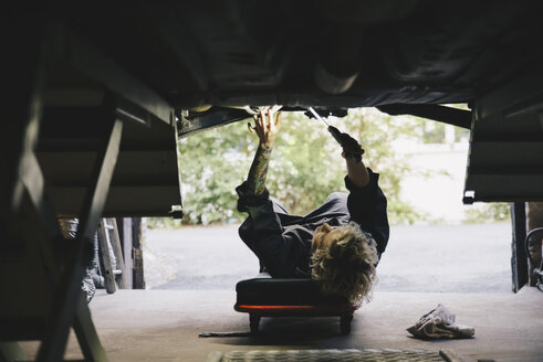 Unteransicht eines weiblichen Mechanikers, der ein Auto in einer Werkstatt repariert - MASF00478