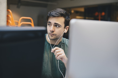 Thoughtful computer programmer wearing in-ear headphones in office stock photo