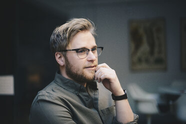 Nachdenklicher männlicher Computerprogrammierer mit Hand am Kinn, der im Büro wegschaut - MASF00486