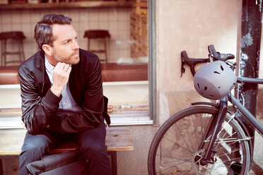 Thoughtful businessman sitting on bench by bicycle at city - MASF00493