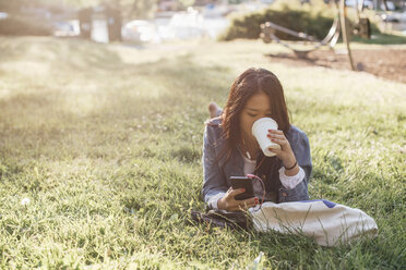 Teenage girl drinking coffee while using smart phone on grass - MASF00501
