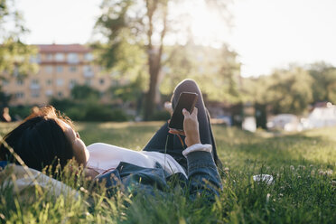 Teenage girl using smart phone while lying on grass - MASF00502