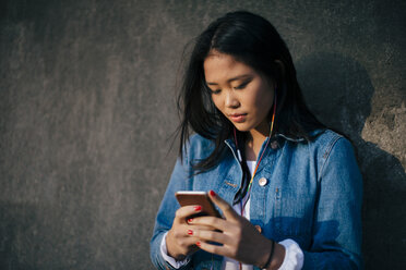 Teenage girl using smart phone while standing against wall - MASF00504