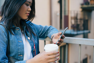 Teenager-Mädchen, das ein Smartphone benutzt und einen Einweg-Kaffeebecher am Geländer hält - MASF00505