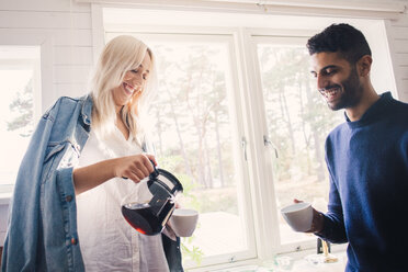 Lächelnde junge Frau, die Kaffee in eine Tasse gießt, während sie bei einem männlichen Freund zu Hause steht - MASF00520