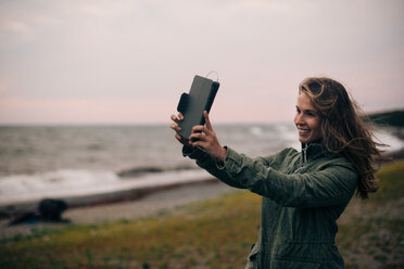 Lächelnde junge Frau, die ein Selfie auf einem digitalen Tablet am Strand macht - MASF00524