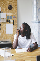 Nachdenklicher junger Geschäftsmann sitzt mit Hand am Kinn am Tisch in einem kreativen Büro - MASF00552