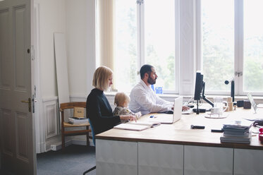 Working mother with daughter sitting by male colleague in office - MASF00553