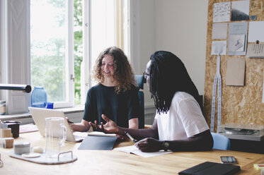 Young businessman and businesswoman discussing over laptop at table in creative office - MASF00556