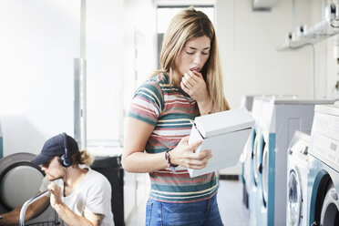 Woman reading information on detergent pack while man using washing machine at laundromat - MASF00560