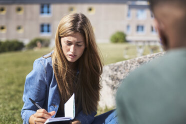 Frau schreibt an einem Buch, während sie mit einem Freund auf dem Universitätscampus sitzt - MASF00562