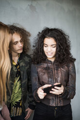 Teenage girl showing mobile phone to friends standing against wall at parking garage - MASF00563