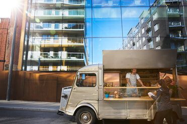 Woman buying food from male owner at food truck on city street - MASF00589