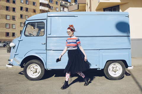Junge Frau, die an einem blauen Mini-Van auf einer Straße vorbeigeht, lizenzfreies Stockfoto