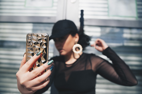 Junge Frau nimmt Selfie mit Smartphone gegen Glastür, lizenzfreies Stockfoto