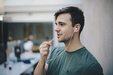 Junger männlicher Computerprogrammierer mit In-Ear-Kopfhörern beim Gespräch im Büro - MASF00609