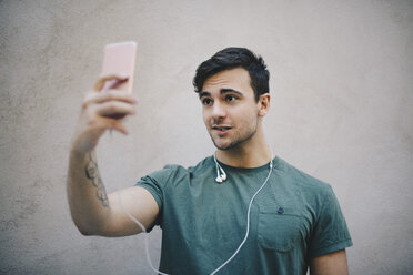 Young male computer programmer taking selfie with smart phone against beige wall in office - MASF00610