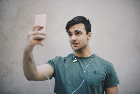 Junger männlicher Computerprogrammierer, der ein Selfie mit seinem Smartphone vor einer beigen Wand im Büro macht - MASF00610