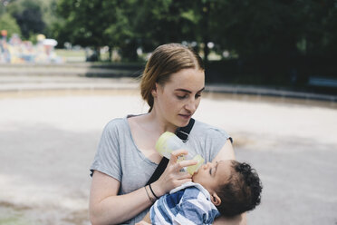 Young mother feeding baby boy from bottle at park - MASF00614