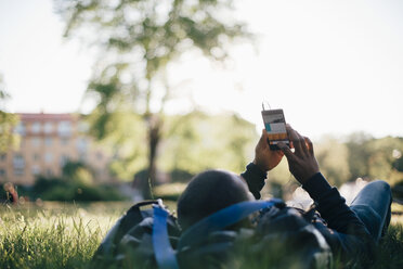 Junger Mann benutzt sein Smartphone, während er im Gras liegt - MASF00626