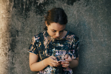 Junge Frau, die ein Mobiltelefon an der Wand benutzt - MASF00627