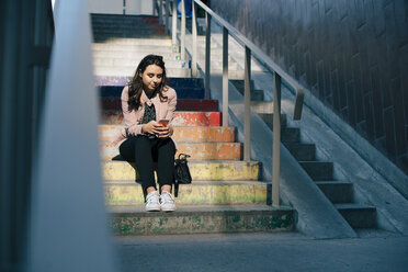 Junge Frau sitzt mit Mobiltelefon auf einer Treppe in der Stadt - MASF00630