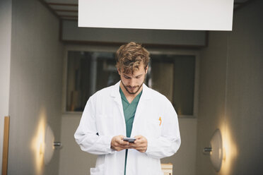 Junger männlicher Arzt mit Mobiltelefon im Krankenhaus - MASF00633