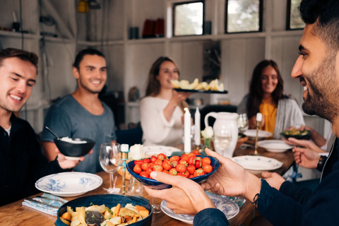 Junger Mann hält eine Schüssel Erdbeeren in der Hand, während er mit Freunden zum Mittagessen zusammensitzt, lizenzfreies Stockfoto