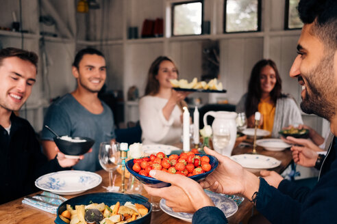 Young man holding bowl of strawberries while sitting with friends for lunch party - MASF00658