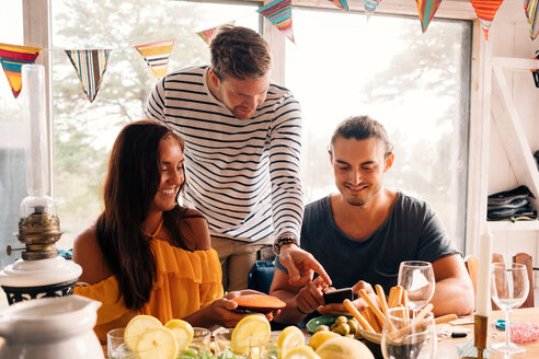 Young men and woman using mobile phone at dinning table - MASF00664