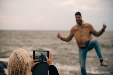 Junge Frau fotografiert Mann auf digitalem Tablet am Strand - MASF00671