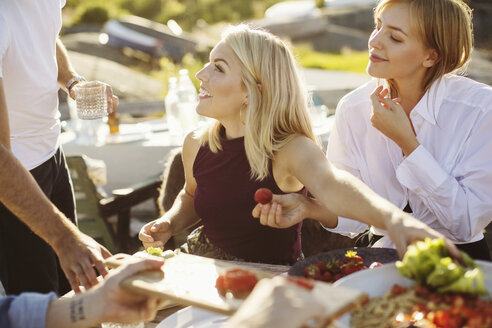 Young multi-ethnic friends with food on table at harbor during sunny day - MASF00677