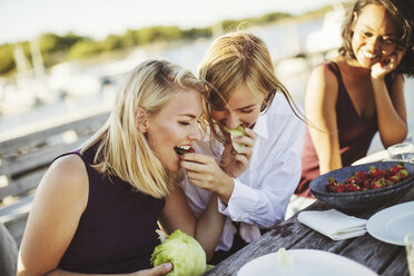 Junge Frau schaut auf fröhliche blonde Freundinnen, die sich am Picknicktisch Kohl teilen - MASF00678