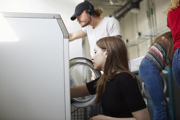 Young male and female friends doing laundry at laundromat - MASF00704