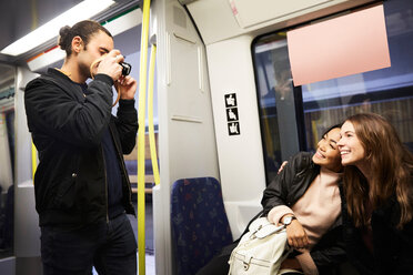 Junger Mann fotografiert glückliche Freundinnen im Zug sitzend - MASF00716