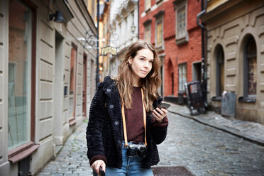 Junge Frau mit Mobiltelefon, die in einer Gasse steht und wegschaut - MASF00718