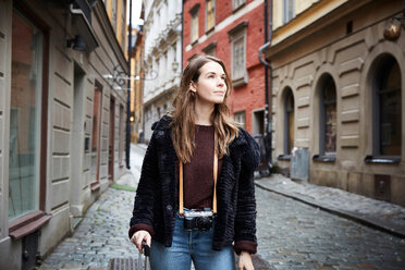 Junge Frau mit Kamera, die wegschaut, während sie in einer Gasse steht - MASF00719