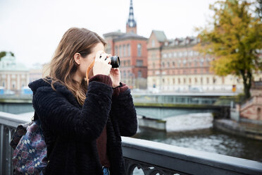 Junge Frau fotografiert durch die Kamera, während sie auf einer Brücke in der Stadt steht - MASF00720