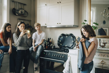 Freunde fotografieren Mädchen mit Stoff durch Smartphone in Küche - MASF00737