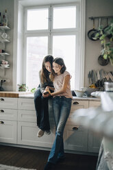 Full length of smiling female friends using mobile phone in kitchen at home - MASF00747