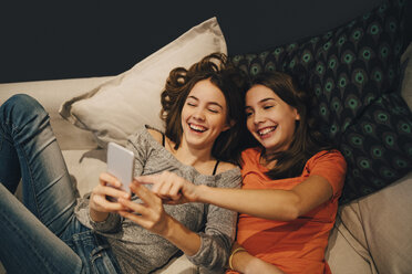 Hoher Blickwinkel von glücklichen Freunden, die ihr Telefon benutzen, während sie sich auf dem Sofa zu Hause ausruhen - MASF00766