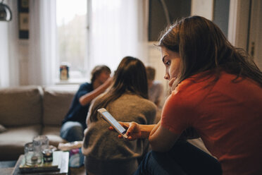 Mädchen benutzt Smartphone, während sie mit Freunden im Wohnzimmer sitzt - MASF00775