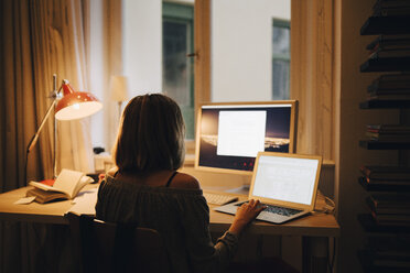 Rear view of girl using laptop and computer while sitting at illuminated desk - MASF00778