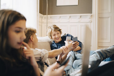 Jungen benutzen ein Mobiltelefon, während sie mit einer Freundin auf dem Sofa sitzen - MASF00783