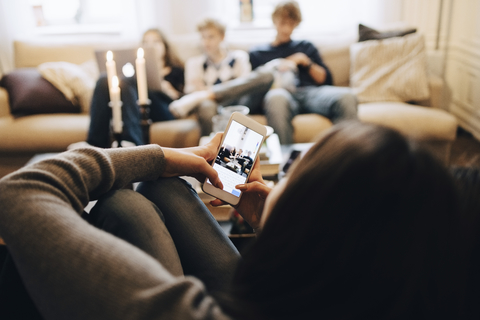 Mädchen fotografiert Freunde, die zu Hause auf dem Sofa sitzen, lizenzfreies Stockfoto