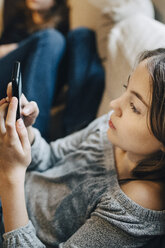 Girl using mobile phone while resting with friend on sofa at home - MASF00793