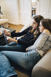 Mädchen benutzen einen Laptop, während sie zu Hause auf dem Sofa sitzen - MASF00797
