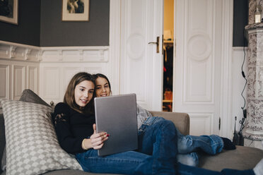 Lächelnde Mädchen, die einen Laptop benutzen, während sie sich auf dem Sofa zu Hause ausruhen - MASF00798